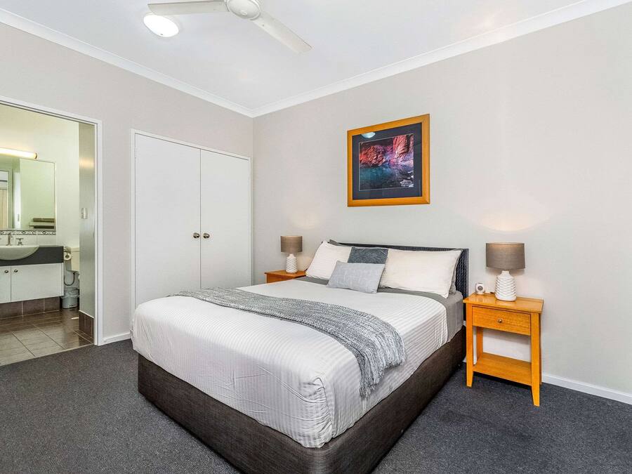A bedroom with a large bed, two bedside tables with lamps, a framed picture on the wall, and a door leading to a bathroom.