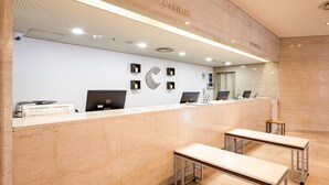 A reception desk with a marble counter, two desks, and a reception area with a ceiling light.