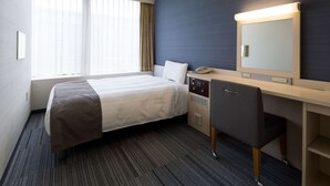 A hotel room with a bed, a desk, a chair, a telephone, and a large mirror.