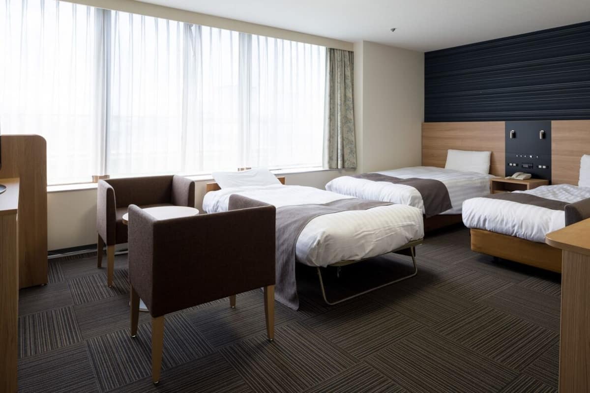 A hotel room with two beds, a desk, a chair, and a large window.