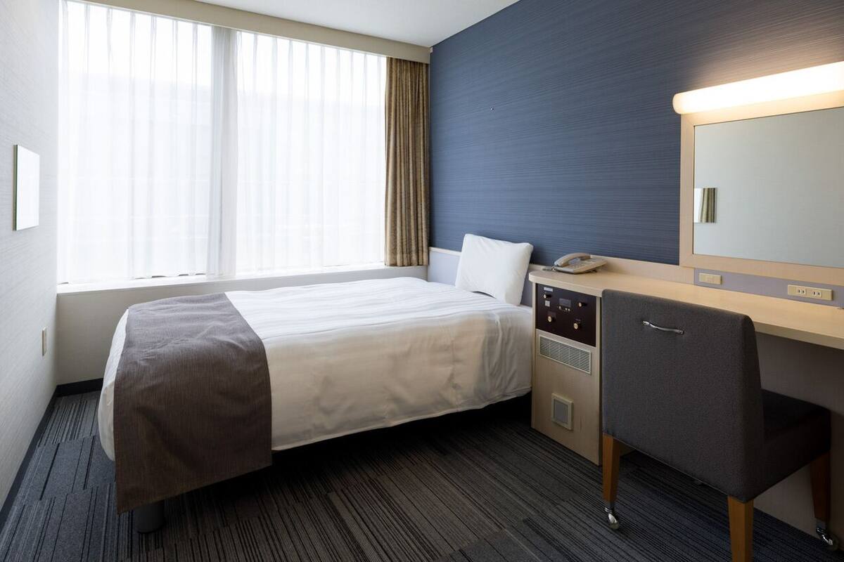 A hotel room with a bed, a desk, a chair, a telephone, and a large mirror.
