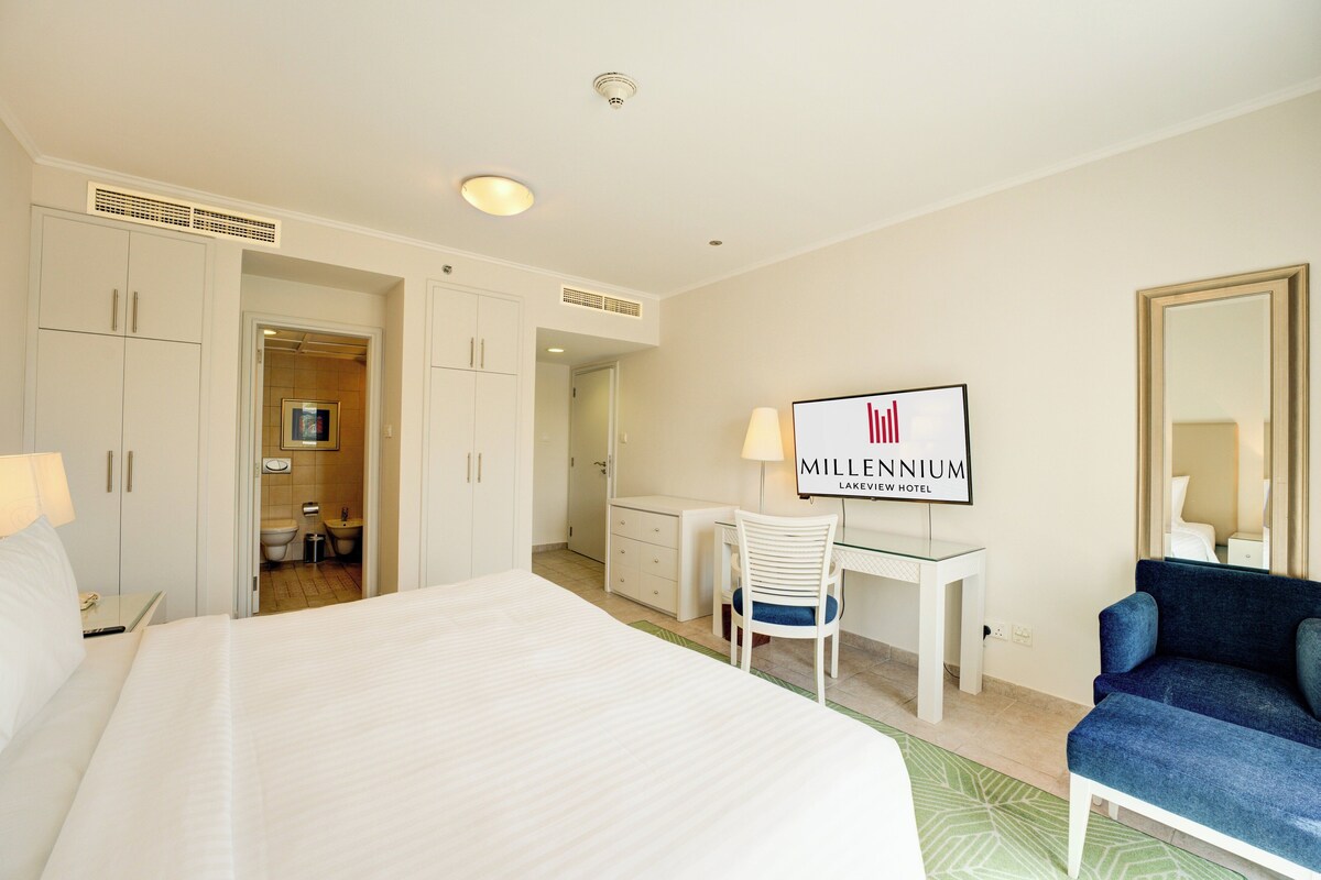 A hotel room with a large bed, a desk, a chair, a TV, and a mirror.
