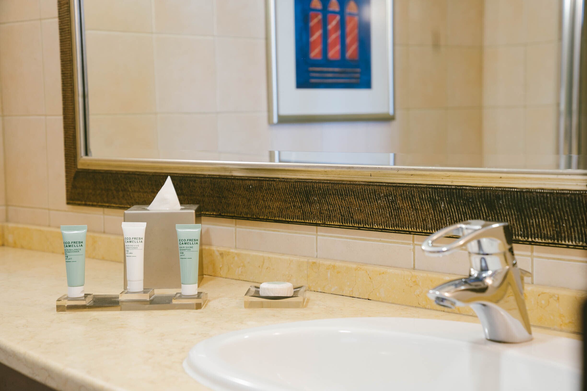 Un lavabo de salle de bain avec un miroir, un porte-serviettes et trois tubes de lotion disposés sur un plateau.