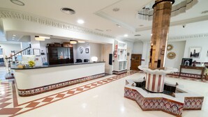 Tilava aula, jossa on vastaanottotiski, suuri pylväs ja kuvioitu lattia.
