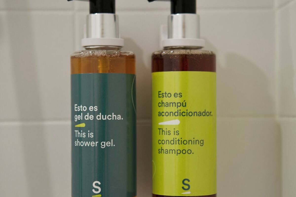 Dos botellas de gel de ducha y champú acondicionador sobre una pared de azulejos.