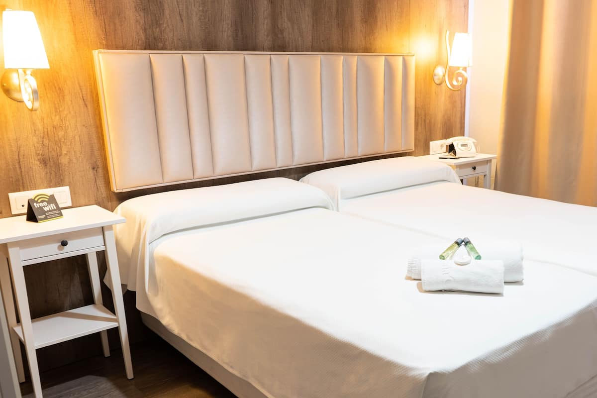 Una cama doble con ropa de cama blanca, cabecera, mesitas de noche con lámparas y un cartel que ofrece WiFi gratuito.