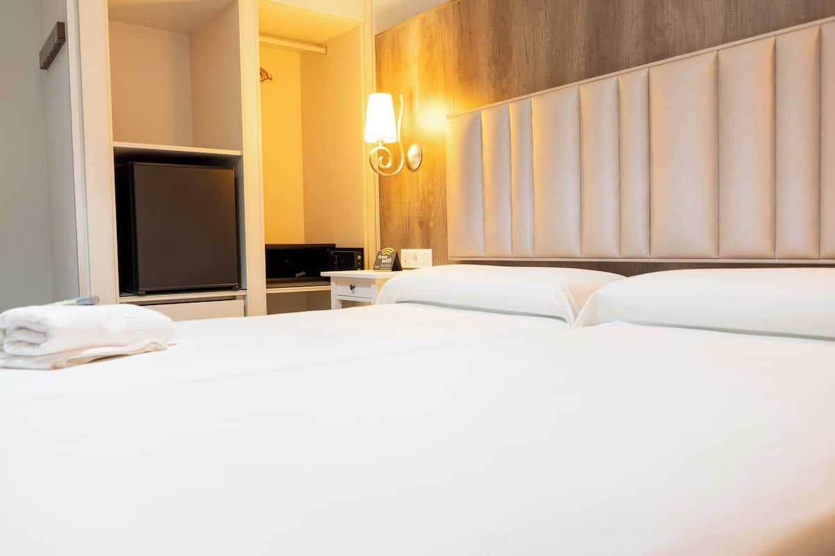Habitación de hotel con una cama grande, televisor de pantalla plana, minibar e iluminación en la pared.