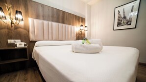 Hotellihuone, jossa on suuri sänky, puinen pääty, seinään kiinnitetyt lamput, puhelin ja kehystetty kuva Eiffel-tornista.