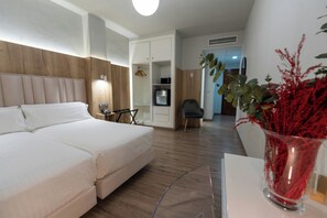 A hotel room with a bed, a desk, a chair, a wardrobe, and a small kitchenette.