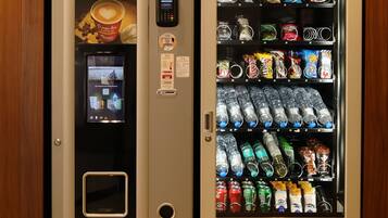 Máquina automática de venda com opções de café e lanches, terminal de pagamento e tela digital.