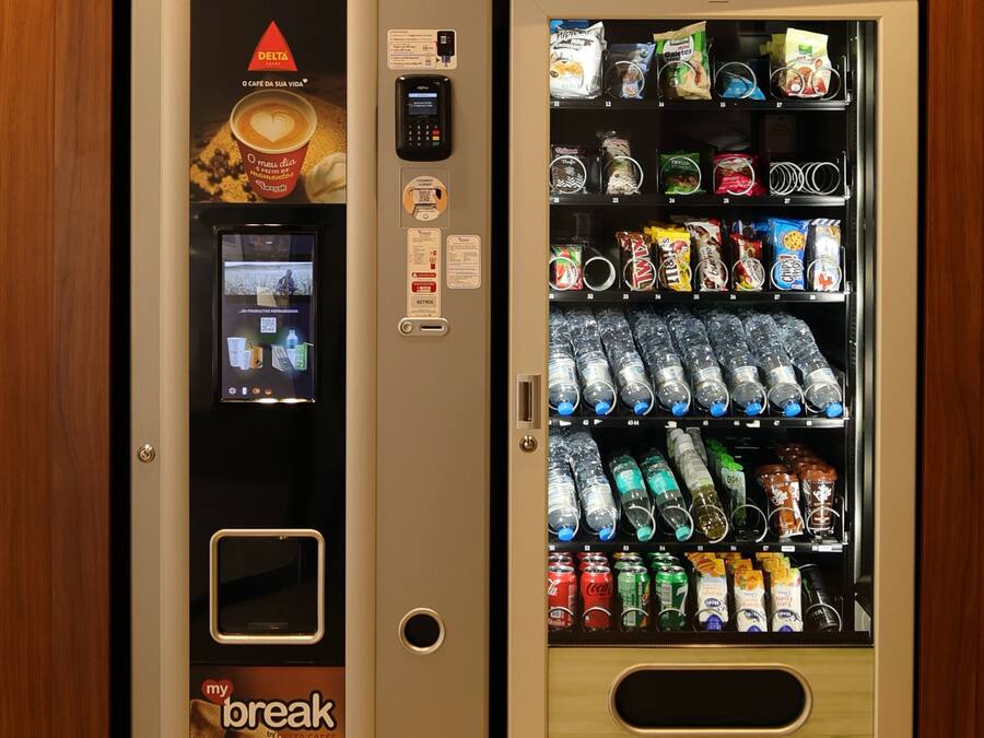 Ein Getränkeautomat mit Kaffe- und Snacksortiment, einem Bezahlsystem und einem digitalen Bildschirm.