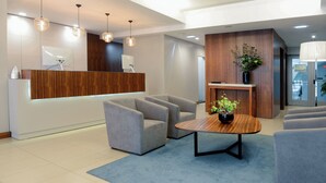 Un área de recepción moderna con un mostrador de madera, sillas tapizadas en gris, una mesa de centro e iluminación colgante.