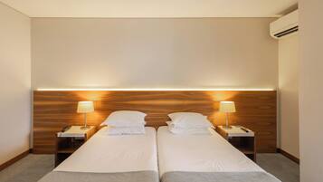 A hotel room with two beds, bedside lamps, a telephone, and an air conditioning unit.