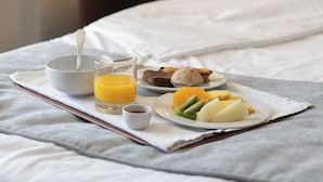 Cama bien hecha con bandeja de desayuno que incluye un tazón, un vaso de jugo de naranja y un plato de fruta y pasteles.