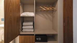 Un vestidor con puertas de madera, una percha, estantes con toallas dobladas y una caja fuerte negra.