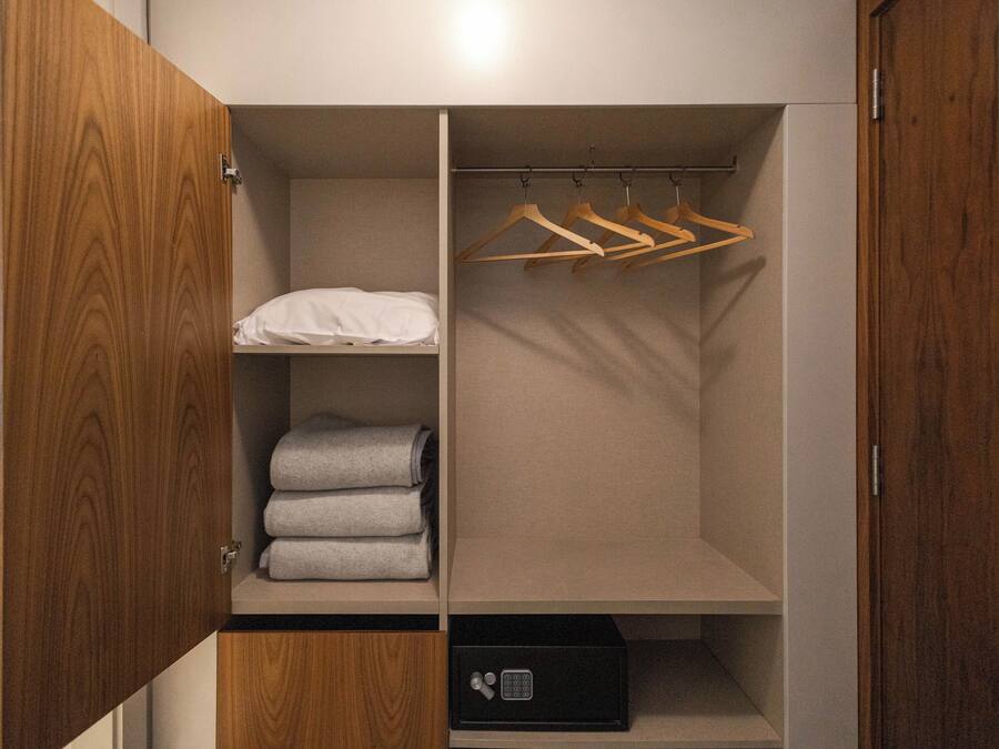 Ein begehbarer Kleiderschrank mit Holztüren, einer Kleiderstange, Regalen mit gefalteten Handtüchern und einem schwarzen Safe.