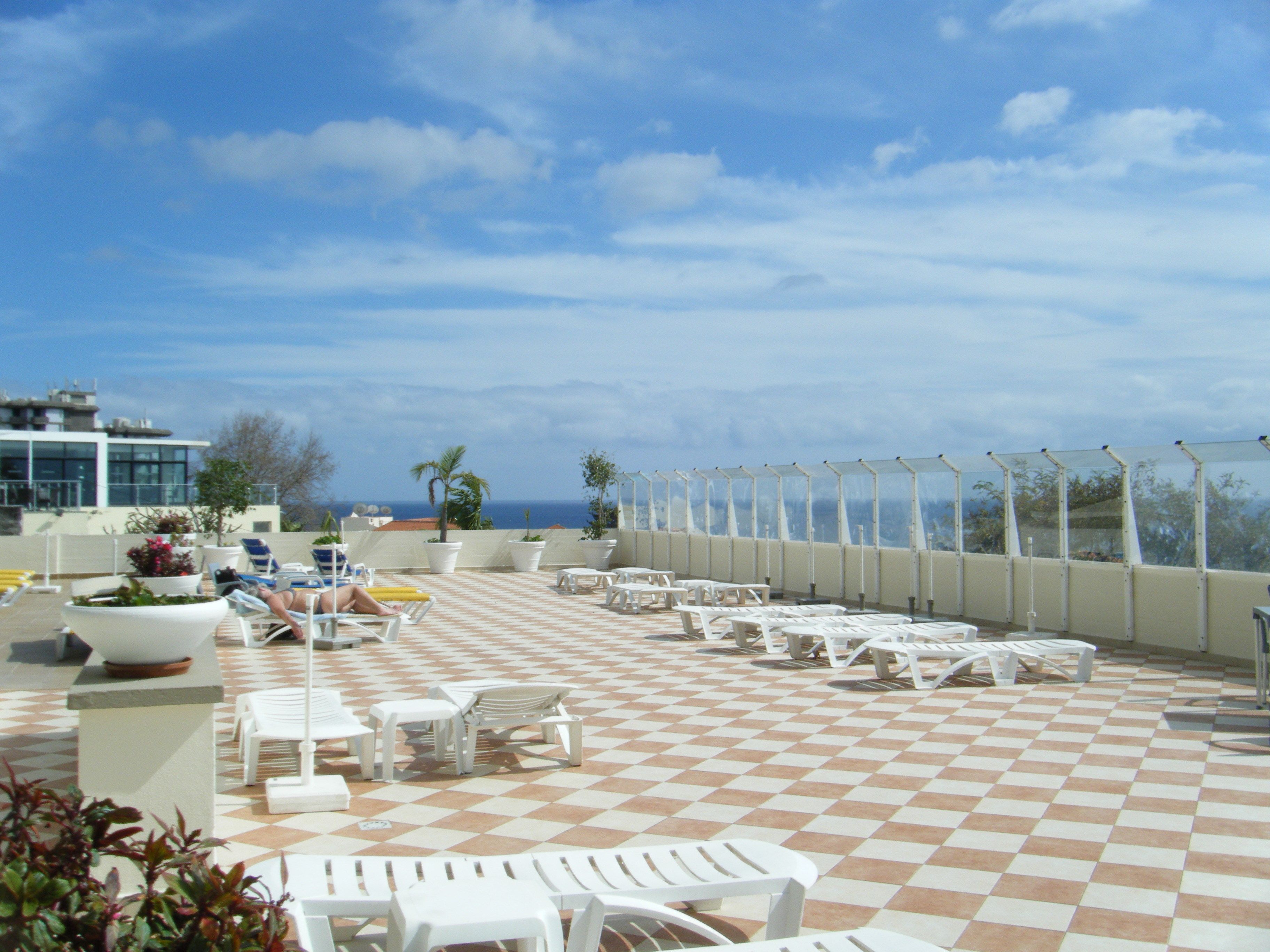 A rooftop terrace with checkered flooring, white lounge chairs, and a view of the ocean.