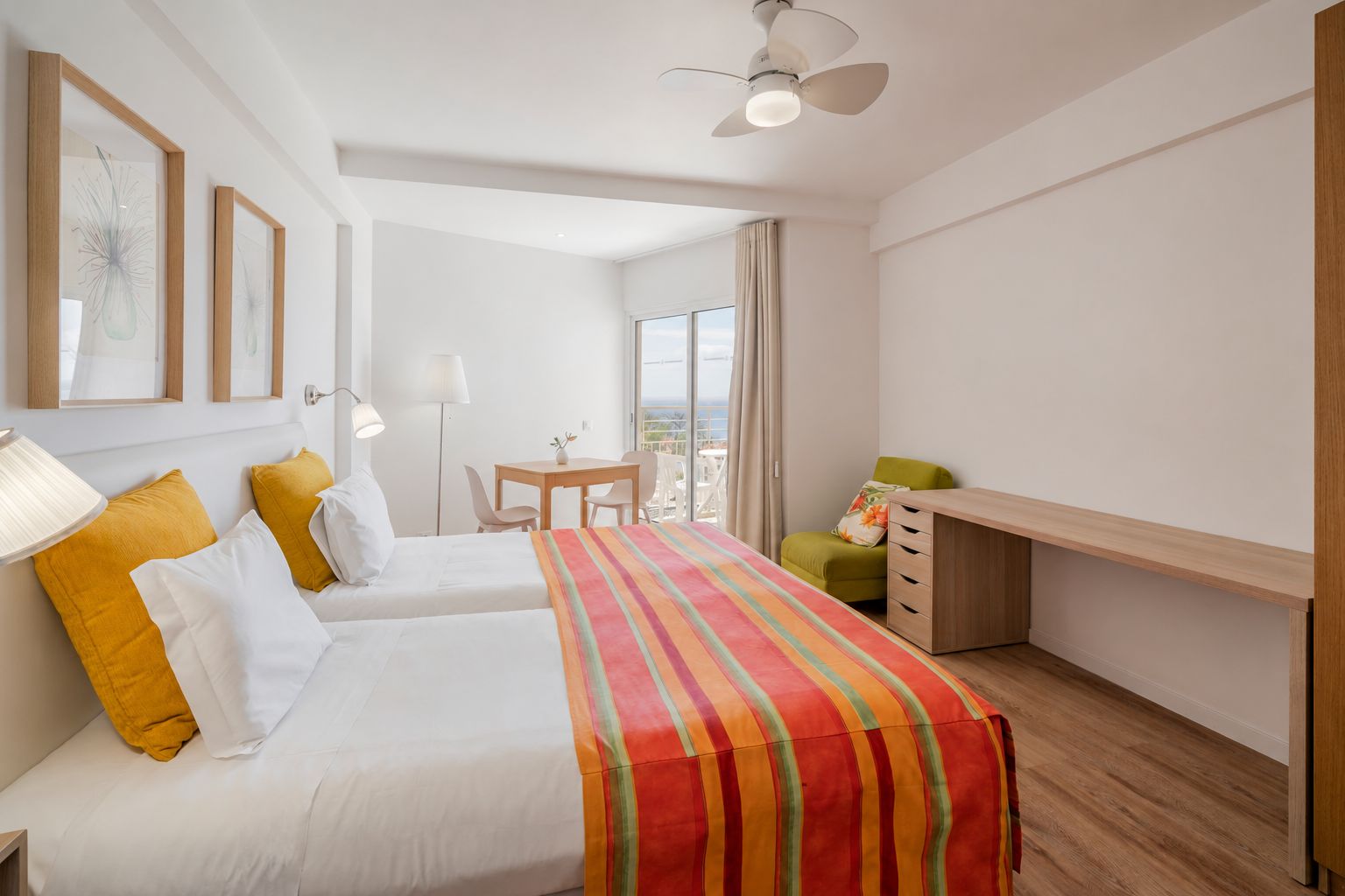 Une chambre d’hôtel avec deux lits, un bureau, une chaise, une lampe et une vue sur l’extérieur.