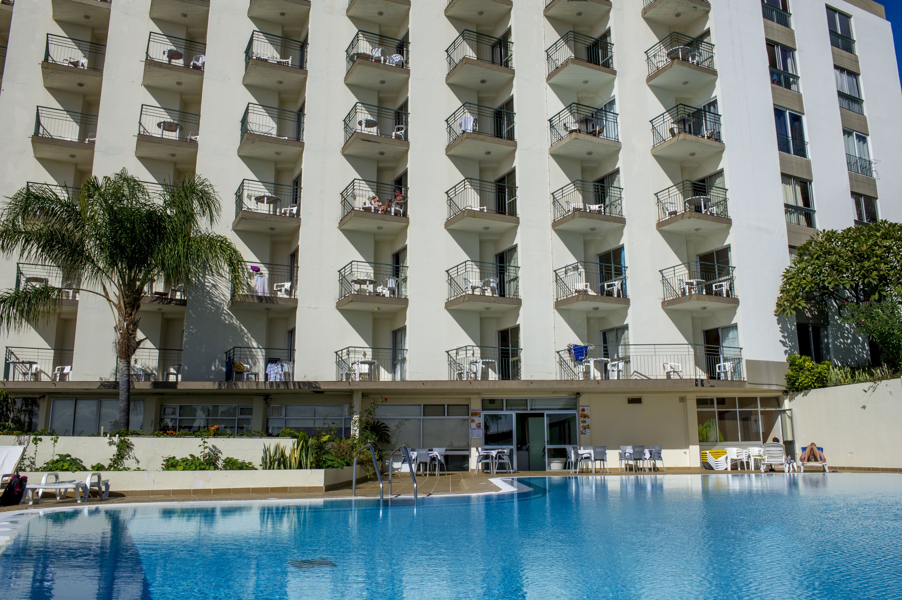 Un hotel de altura con piscina, varios balcones y zonas de estar al aire libre.
