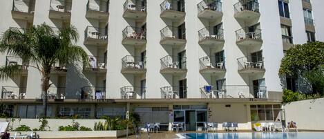 A high-rise hotel with a swimming pool, multiple balconies, and outdoor seating areas.