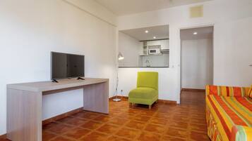 A modern living room with a flat-screen TV, a green armchair, a sofa with a striped cover, and a kitchen area in the background.
