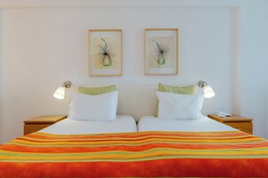 Ein Doppelbett mit gestreifter Decke, zwei Kissen, zwei Nachttischlampen und zwei gerahmte Pflanzenbilder an der Wand.