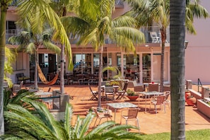 A hotel courtyard with outdoor seating, palm trees, and a view of the building's interior. - Florasol Residence Hotel (Funchal)