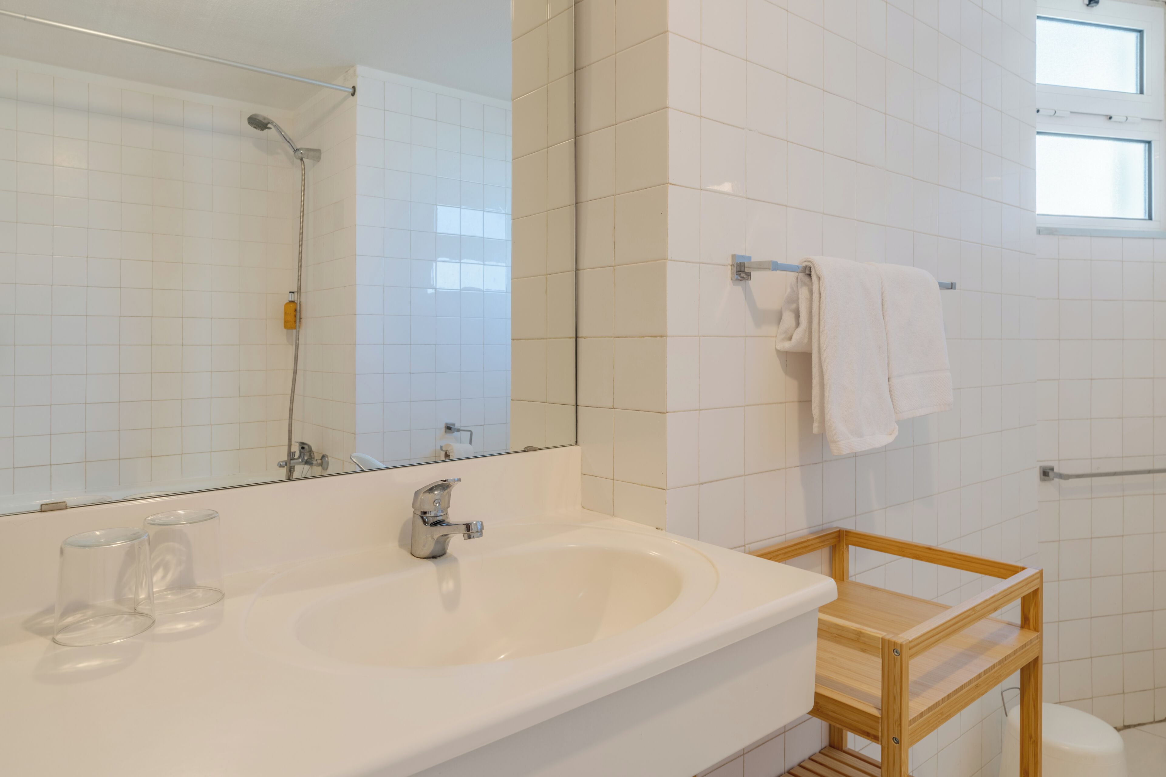 Un baño con lavamanos blanco, un espejo, ducha y tocador de madera.