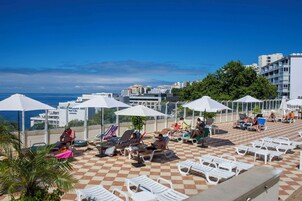 Een dak terras met ligbedden en parasols, met uitzicht op een stadsbeeld en de zee.