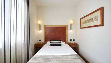 Quarto de hotel com uma cama grande, duas mesas de cabeceira, um painel de cabeceira de madeira, uma obra de arte emoldurada na parede e uma janela com cortinas translúcidas.