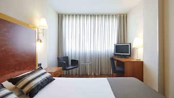 Habitación de hotel con una cama grande, un escritorio con computadora, una silla, una mesita y un televisor.