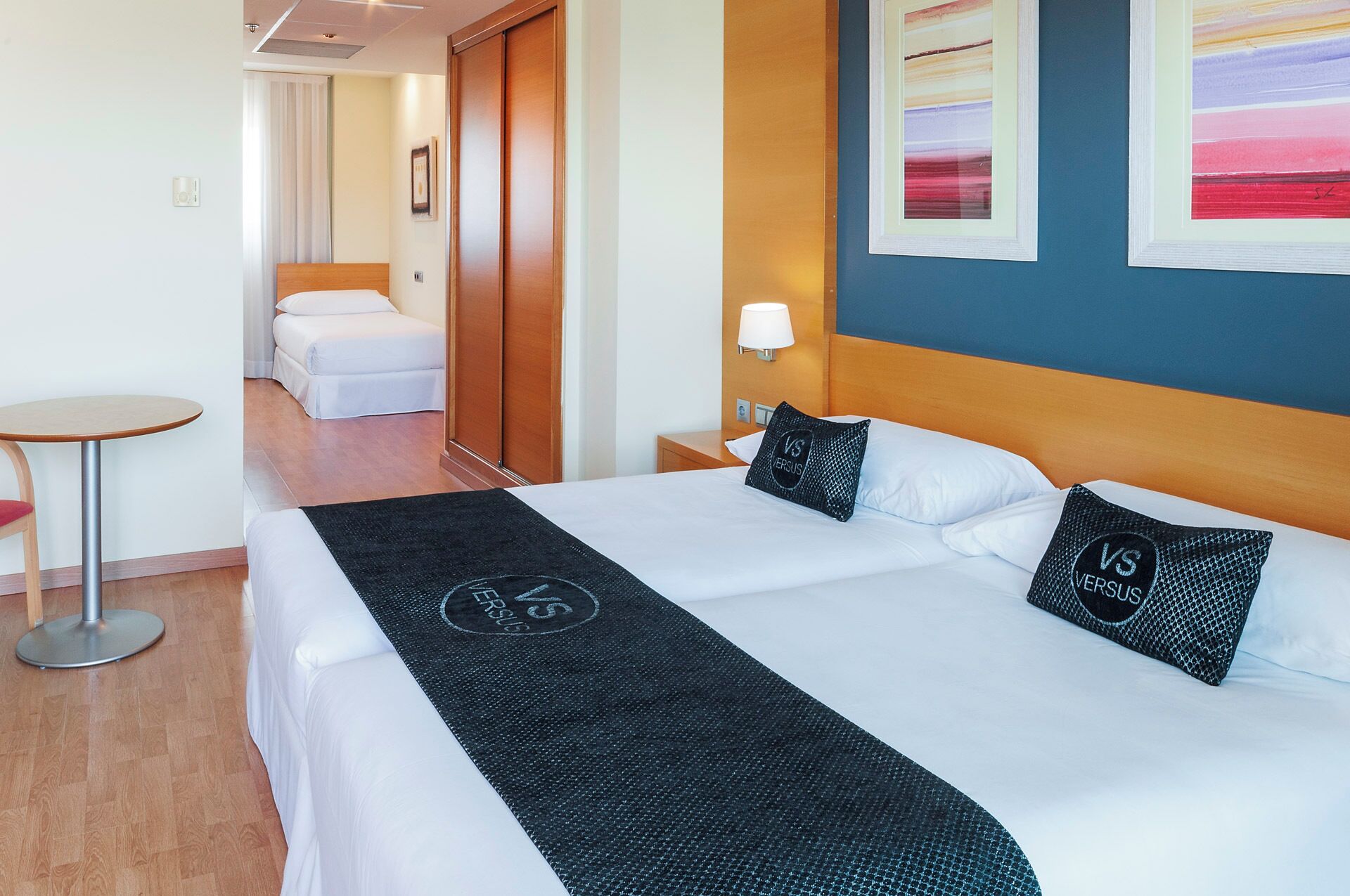 A hotel room with a large bed, a small table, and a nightstand with a lamp.
