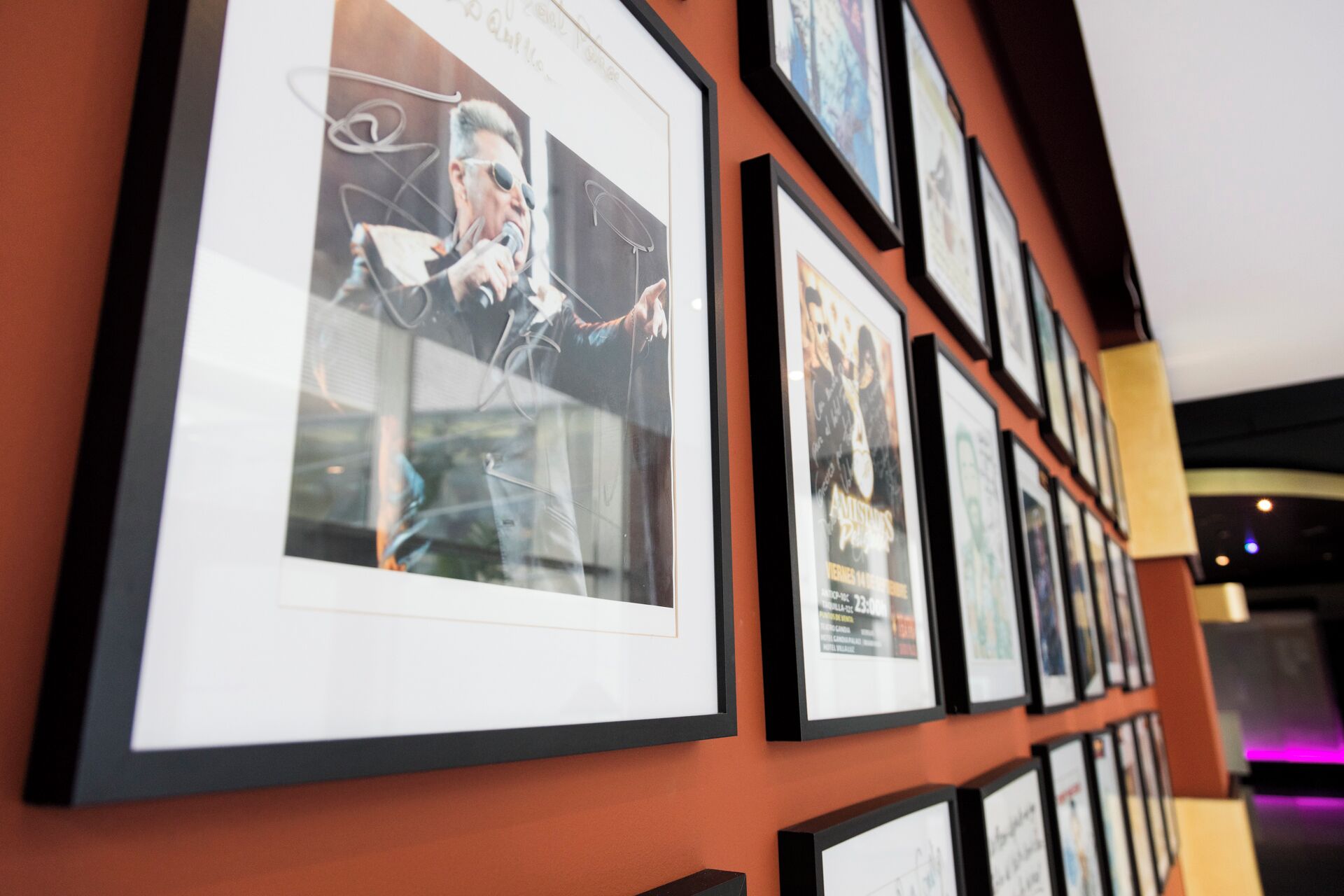 Un mur orné de plusieurs tableaux encadrés, dont une affiche représentant une personne tenant un microphone.
