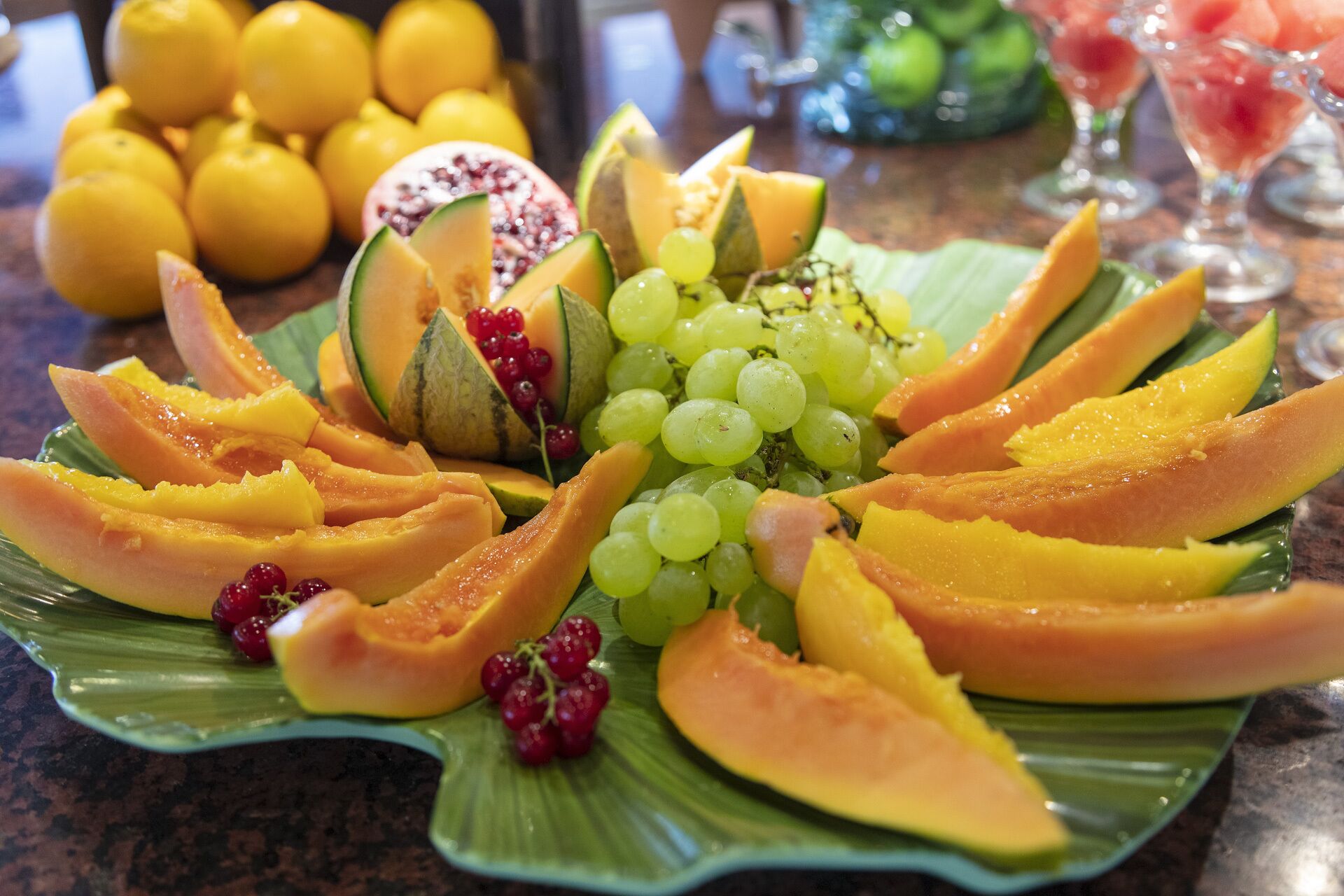 A fruit platter with sliced papaya, mango, and grapes on a green leaf plate.