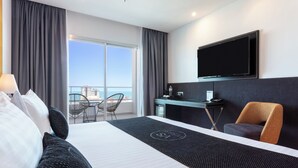 Habitació d'hotel amb un llit gran, una taula, una cadira, televisió i un balcó amb vista al mar.