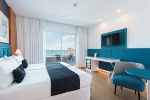 Habitación de hotel con cama, escritorio, silla, televisor y balcón con vistas.