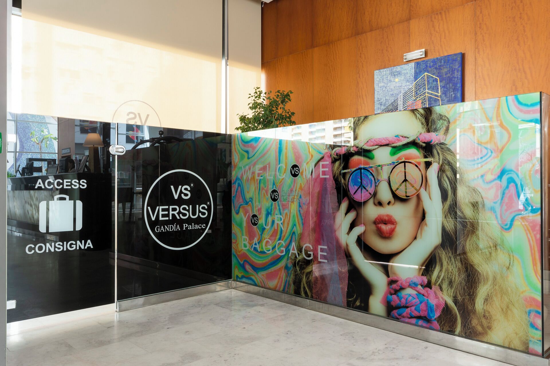 Un área de recepción con una pared de vidrio que muestra un anuncio colorido y el logotipo de 'VS VERSUS GANDÍA Palace'.