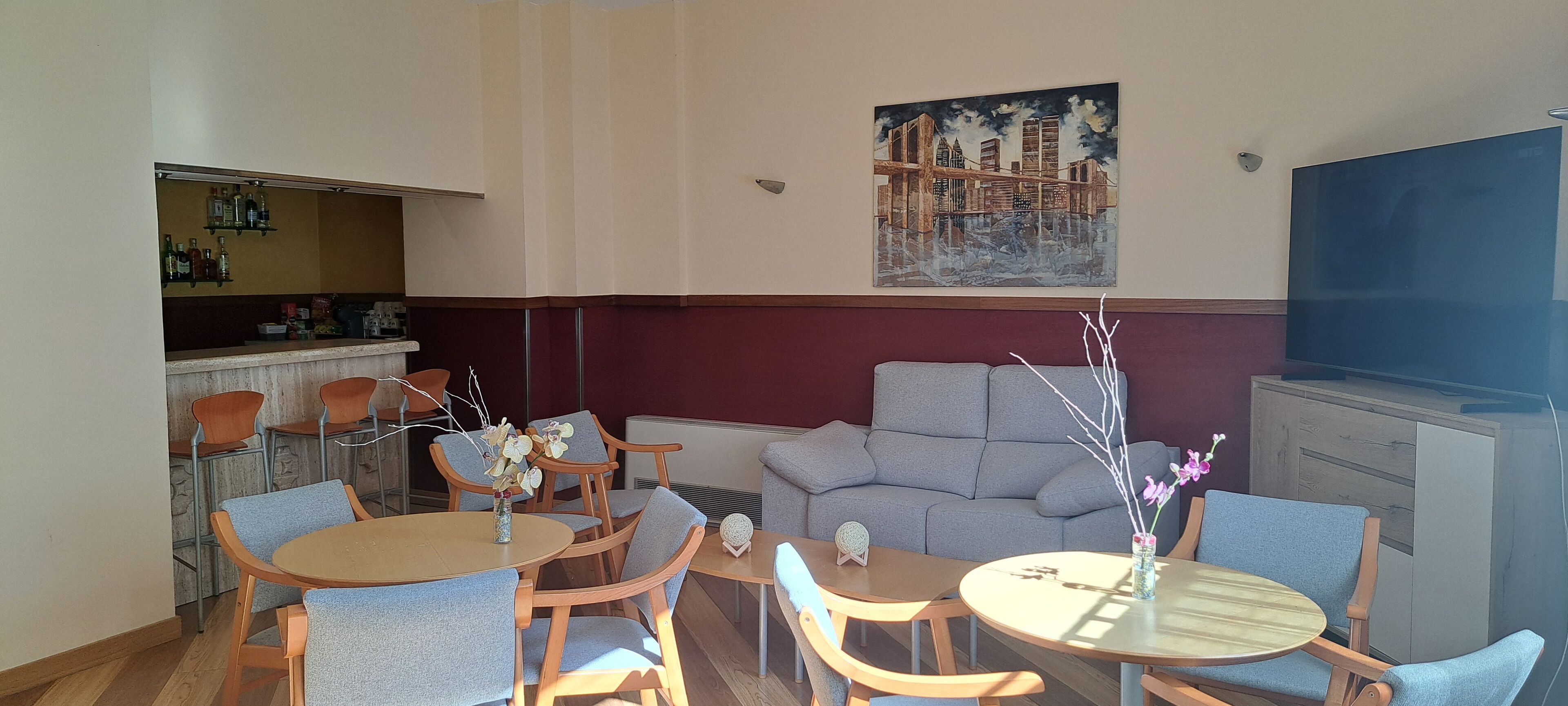 A dining area with round tables and chairs, a sofa, a TV, and a painting on the wall.