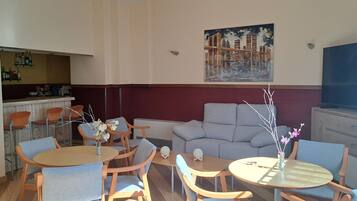 A dining area with round tables and chairs, a sofa, a TV, and a painting on the wall.