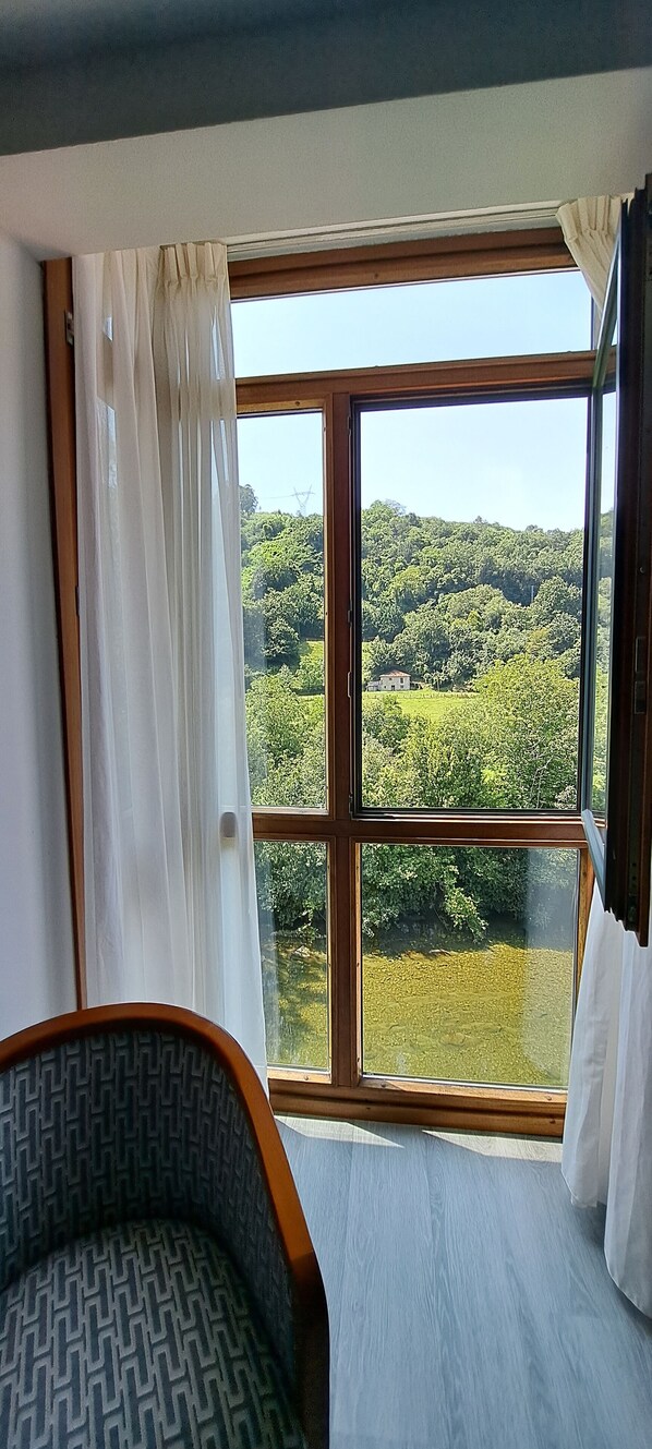 Una habitación con un ventanal grande, una silla estampada y vistas a un paisaje verde.