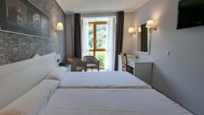 Et hotelværelse med stenvæg, to senge, et skrivebord, en stol og et fjernsyn.