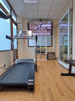 A gym with a treadmill, weights, and a TV displaying a sports event. - Hotel Ciudad Cangas De Onis (Cangas de Onis)
