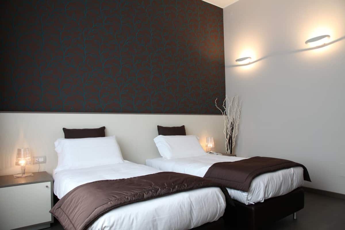 Hotellihuone, jossa on kaksi sänkyä, tumma kuvioitu seinä ja seinään asennetut valaisimet.