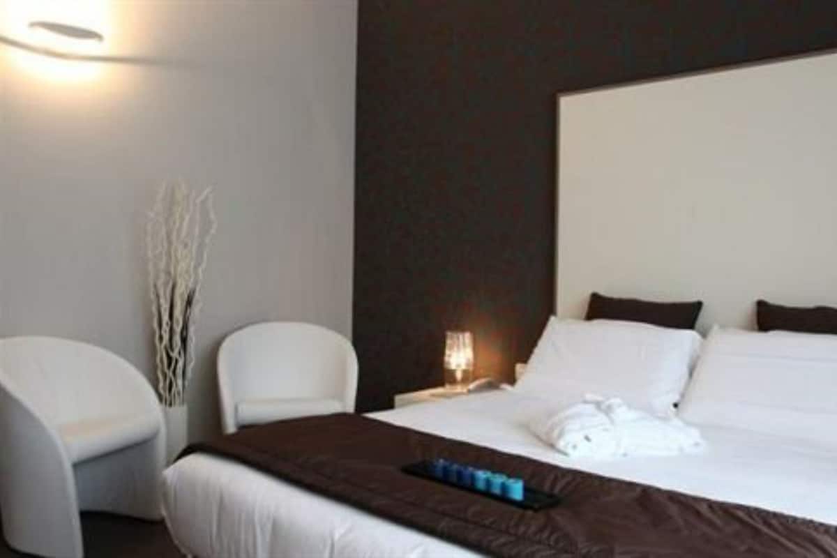 Hotellihuone, jossa on suuri sänky, kaksi valkoista tuolia, yöpöytä lampun kanssa ja koristeellinen oksa seinällä.