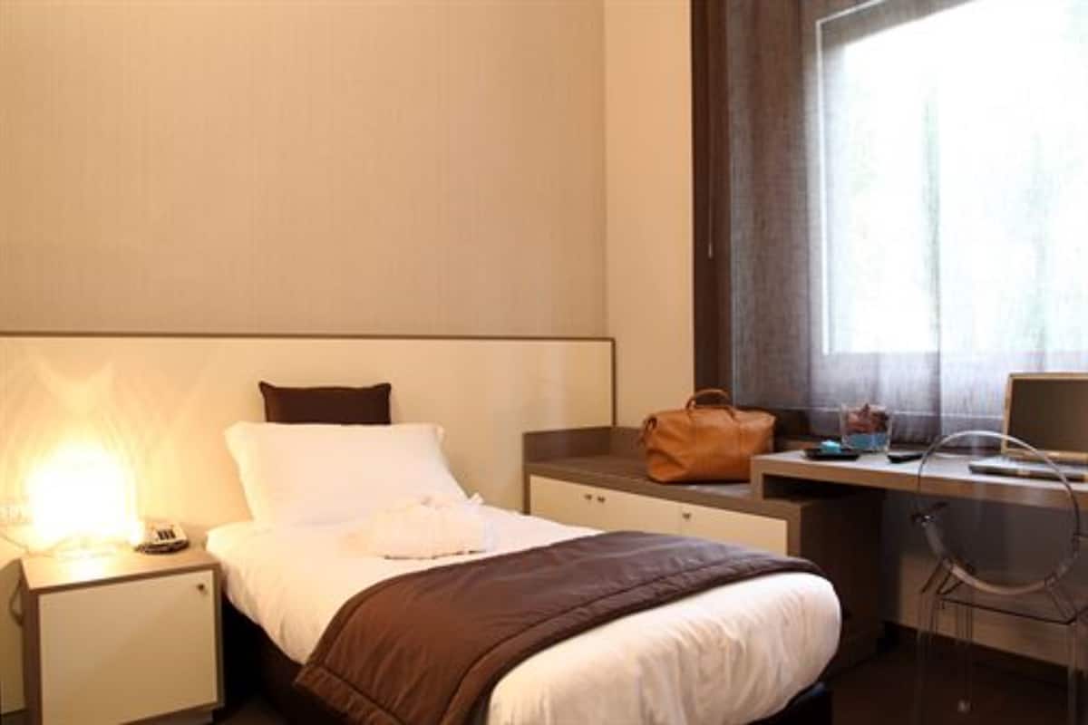 Hotellihuone, jossa on sänky, yöpöytä, lamppu, työpöytä, tuoli ja ikkuna.