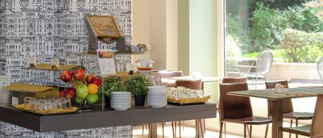Un comedor con mesas de buffet, que incluye frutas, platos y vasos.