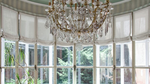 A room with a large bay window, a chandelier, and a round table. - Hotel Tiziano (Milan)