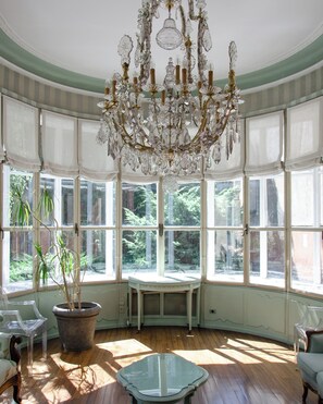 A room with a large bay window, a chandelier, and a round table. - Hotel Tiziano (Milan)