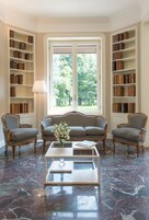 Una biblioteca con un divano decorato, due poltrone e un tavolino in marmo.