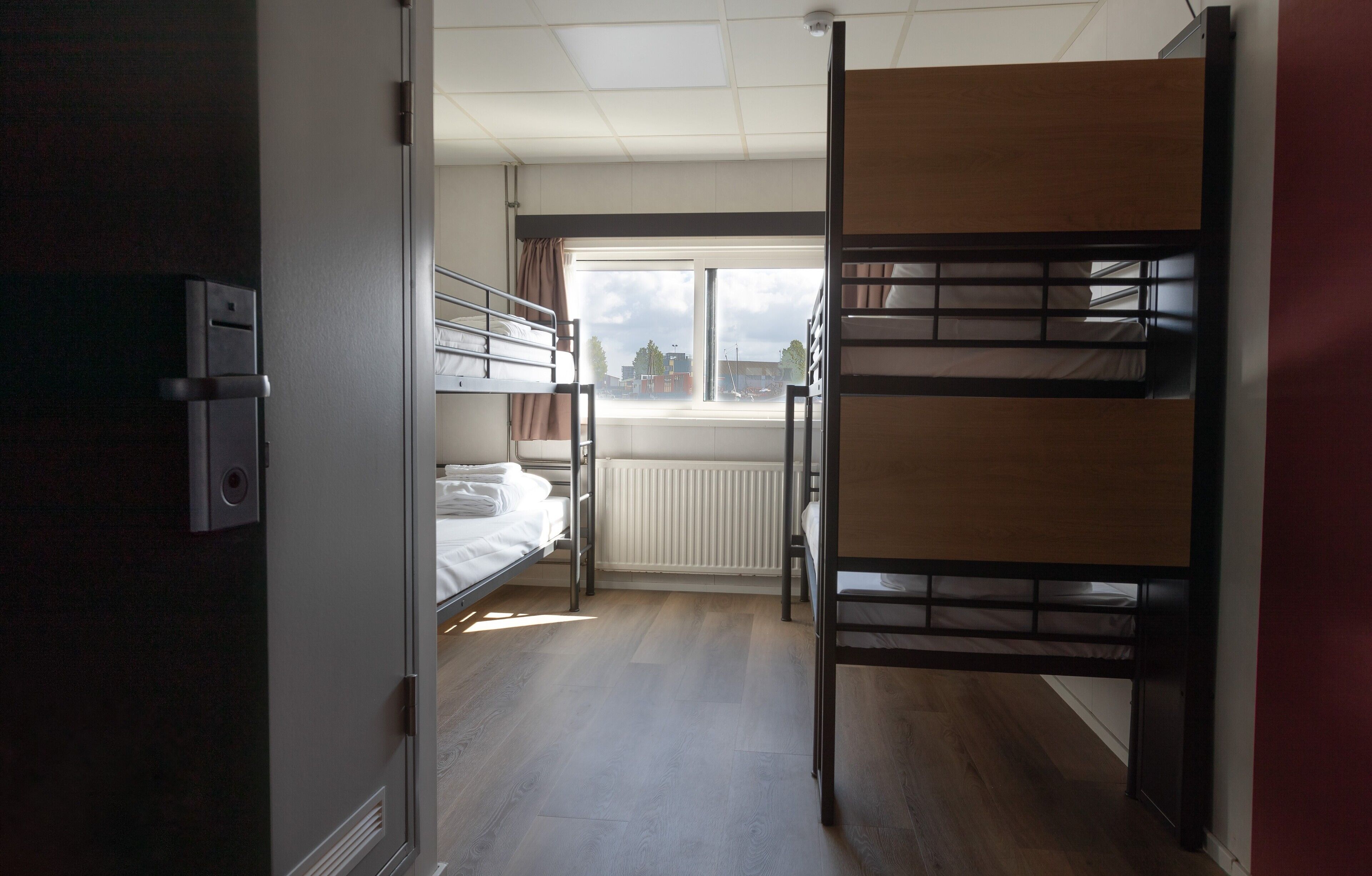 A room with bunk beds, a radiator, and a window with a view of buildings.